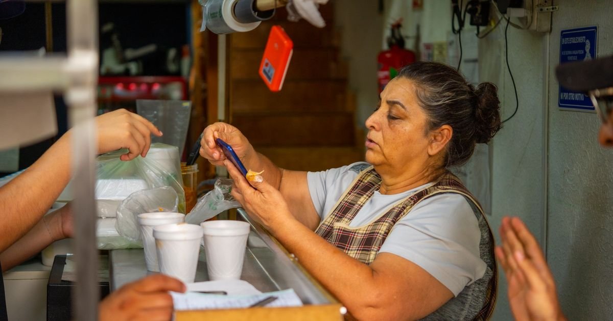 Vendedora de un puesto de comida revisa su celular mientras atiende a sus clientes.